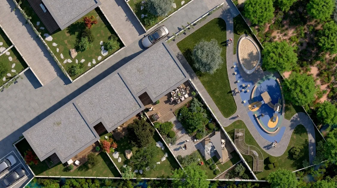 İki villa arasındaki bahçe aksının tepeden görünümü: taş döşeli avlular, ahşap teras üzerinde yemek masası, sağda oyun alanı ve kaykay rampası